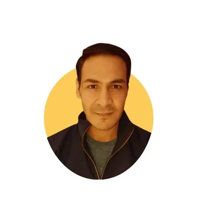 Portrait of Akhand Pratap Singh, an Indian fitness enthusiast and transformation coach, smiling confidently at the camera while flexing his well-defined arms, chest, and six-pack abs in a gym setting. He has short dark hair, a beard, and is wearing a sleeveless black tank top